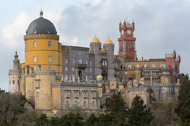 Fachada amarela e vermelha do Palácio Nacional da Pena vista do terraço, com a serra de Sintra em fundo